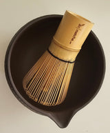 Bamboo whisk and black bowl on a beige background