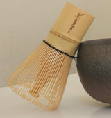 Dark ceramic bowl and whisk on a light surface with a neutral background