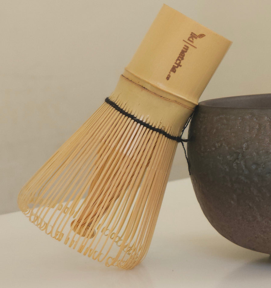 Dark ceramic bowl and whisk on a light surface with a neutral background