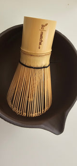Bamboo whisk and black bowl on a light background
