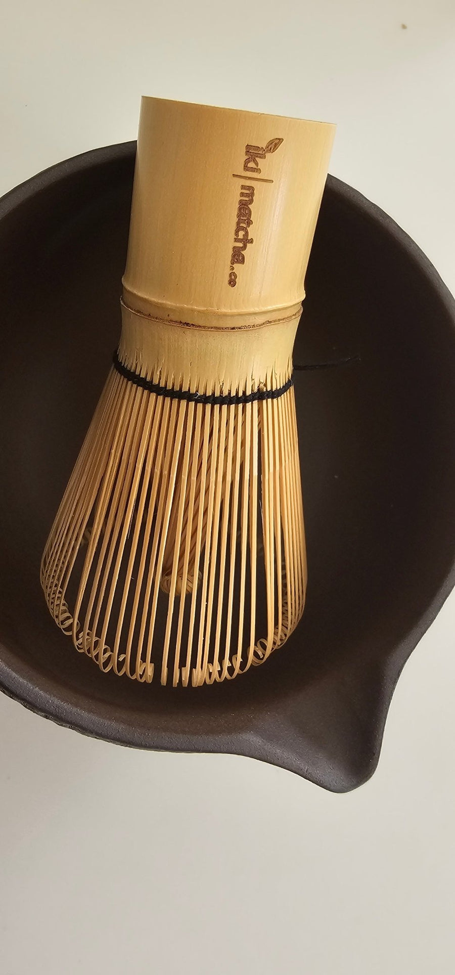 Bamboo whisk and black bowl on a light background